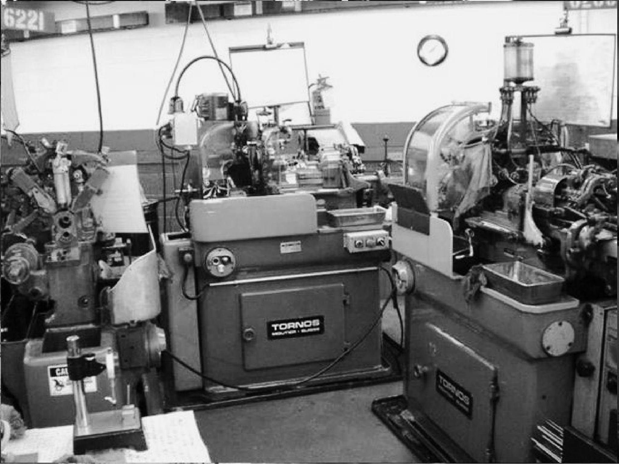 A black and white photo showcasing a set of Tornos Swiss Cam machines in a manufacturing facility. The image displays the machines arranged in a squared-in formation, indicating a well-organized workspace. The Tornos equipment is used for precision machining, highlighting the technical capabilities and specialization of the facility.